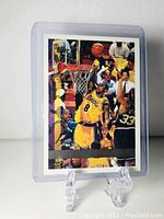 Photo of the front of the Kobe Bryant Topps basketball card in plastic sleeve on display stand.