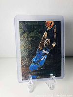 Two photographs of the Kevin Garnett 1996-97 Fleer Metallized basketball card front sides in protective plastic holders. Cards display a metallized finish with the player mid-jump and blue Timberwolves uniform.