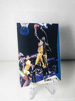 Front view of Kevin Garnett rookie basketball card in protective sleeve and stand, showing player dunking with teammates and opponents.