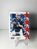 Front view of Tom Brady Score football card showing him in Patriots uniform with stars and Captains logo.