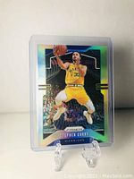 Front side of 2019-2020 Panini Prizm Stephen Curry basketball card showing on-stand display with reflective holographic surface, Stephen Curry in yellow Warriors uniform performing a jump shot.