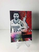 Front view of Jamal Murray basketball card in a clear protective sleeve on an acrylic stand, showing the player's portrait and action shot with red and orange geometric background.