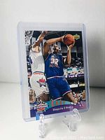 Front of Shaquille O'Neal All Star rookie card showing him in blue East team uniform taking a basketball shot during a game.