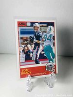 Front of the 2019 Panini Score Tom Brady football card in protective sleeve on clear stand.