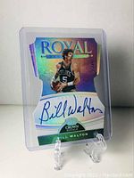 Front view of the Bill Walton autographed die cut card standing upright on a clear display stand.