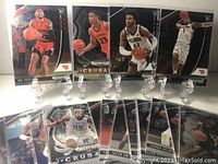 Photo showing 8 basketball rookie cards propped on clear stands with players in various action poses, including ball handling and shooting.