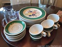 View of stacked dinner plates, saucers, cups, and two small glass pitchers on table