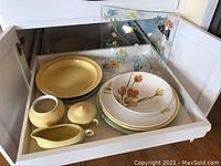 Photo showing the yellow Bauer plate, GMBC sugar bowl with lid, gravy boat, Daphne Ironstone bowl and platter, and Dorothy C. Thorpe hand painted square glass platter inside a cabinet drawer.