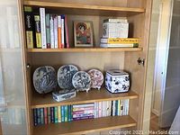 Wide view of wooden bookshelf displaying books, Nymolle plates, trinket box and Kleenex cover