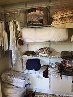 View of multiple bedding and textile items on shelving including a Diamond Peak down comforter, folded linens, and floral pillows.