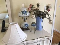 Photo showing full lot with hurricane lamp, pottery vase with faux roses, glass paperweight on stand, candle, and two fabric shades on a white dresser