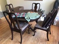 Wooden dining table with four chairs around it, table has items on top: tablecloths and pads.