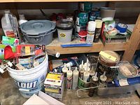 Wide view showing various paint containers, caulking tubes, and painting supplies on shelves and floor.