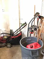 Photo showing Earthwise electric lawn mower with long red power cord coiled on top, black collection bag, wooden ladders in background, and buckets/containers on floor.