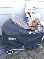 Full view of covered Weber grill with cover logo and wheels visible