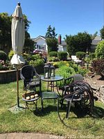 Wide shot of the brown metal bistro table with textured glass top, four plastic chairs, garden hose coiled on chairs, umbrella stand with umbrella, two lanterns on table