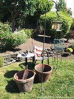 View of garden items together on grass showing metal bird bath, two terracotta pots, plastic chair, and iron bird sculpture.