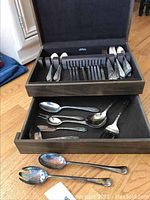 Photo showing silverware stored in a black case including spoons, forks, and serving utensils with two pieces outside the case.