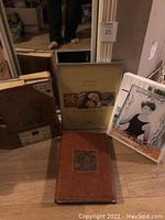 Three photo albums and one glass frame in box, all placed on floor against wall. Two albums still sealed in plastic packaging.