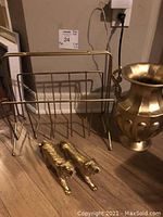 Wide view of gold colour magazine holder, metal vase, and two decorative tigers on floor near wall and power outlet