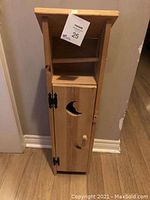Front view of the wooden outhouse style toilet paper holder with cabinet door closed, showing crescent moon cutout and knob.