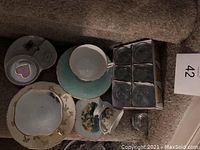Full lot of teacups, saucers, porcelain plate, and shooter glasses displayed on carpeted stairs.