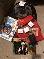 Photo showing camouflage backpack, art project books including Hands Up Art Activities and How to Draw Horses & Ponies, horse-themed agenda, red zipper cloth bag, three boxes of push pins, untested calculator, and two pencil sharpeners in package.