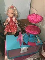 Doll sitting on teal base with pink and blue swirling chair