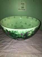 Front angled view of white ceramic bowl with hand painted green leaves and purple berries raspberries decoration, no chips or cracks visible.