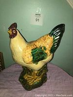 Front and side view of the vintage pottery hen figurine showing cream, green, brown, and black glazed ceramic with textured feathers and a base.