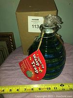 Photo of blue/green ribbed glass wasp trap jar with a tag and measuring tape showing approximately 8 inches tall.