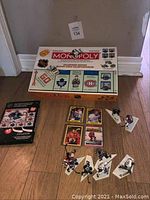 Full lot image showing the NHL Monopoly board game box with dice, game cards, and eight hockey player figures on the floor.