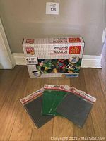 Full view of the Block Tech building blocks box standing on floor next to four unopened base plate packages in green and gray.