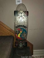 Front view of the FlameBoy Wet Willy skateboard showing multicolored graphic with flames and wheels on clear plastic deck and black wheels.