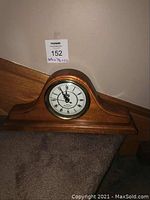 Full view of wooden mantel clock showing its classic rounded top wooden case and placement on a carpeted stair landing.