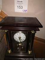 Full view of E & T rotating battery-operated table clock in wooden case with brass accents