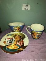 Photo showing the mug, bowl, and plate with front-facing vintage Kellogg's Corn Flakes advertising graphics on the items.