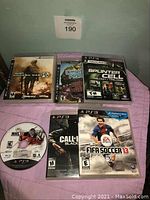 Seven PS3 game cases and discs laid out on a purple surface with titles visible, including two copies of Modern Warfare 2 and one loose NHL 14 disc.