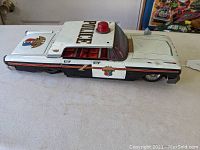 Side view of vintage tin lithograph police car showing original police graphics, red siren light on roof, and black and white color scheme.