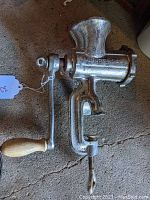 Full side view of cast iron food grinder showing feed tube, crank with wooden handle, and table clamp.