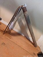 Full view of the clam digging fork showing entire length and structure leaning against the wall on wooden floor.