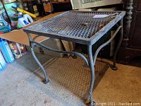Side angle showing the wrought iron mesh top, curved legs, and round feet of the occasional table.