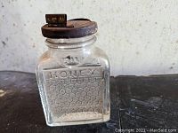 Front and side view of clear square glass jar embossed with 'Pure Honey' and honeycomb pattern, with metal lid.