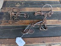 Three distinct wrought steel tavern puzzles shown on wood surface, featuring interconnected metal rings and bars for puzzle challenge.