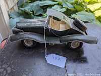 Side view of the handcrafted vintage-style metal car model showing green body, rounded fenders, fabric seats, and intricate details on the hood and wheels.