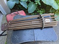 View of the drying rack folded on a table outside with garden plants in the background, showing the wooden slats and iron framework.
