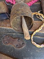 Close-up of large metal bell with wooden clapper and braided yellow and red rope.