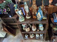 Wide view of shelf containing multiple collectible decanters of ceramic animals including duck, bear, rabbit, and bird shapes; small ceramic jugs and mugs; glass decanter