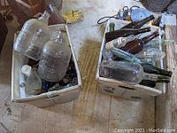 Two white bins filled with a mix of mostly dug glass bottles in various colors and sizes, showing two large embossed jugs on top.