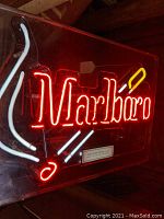 Front view of illuminated neon sign showing red 'Marlboro' text with white smoke lines and yellow-white lit cigarette design.